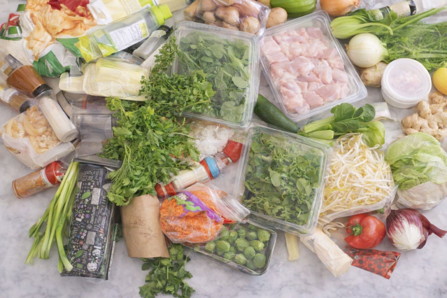 Et udvalg af friske ingredienser fra en måltidskasse spredt ud på et bord.